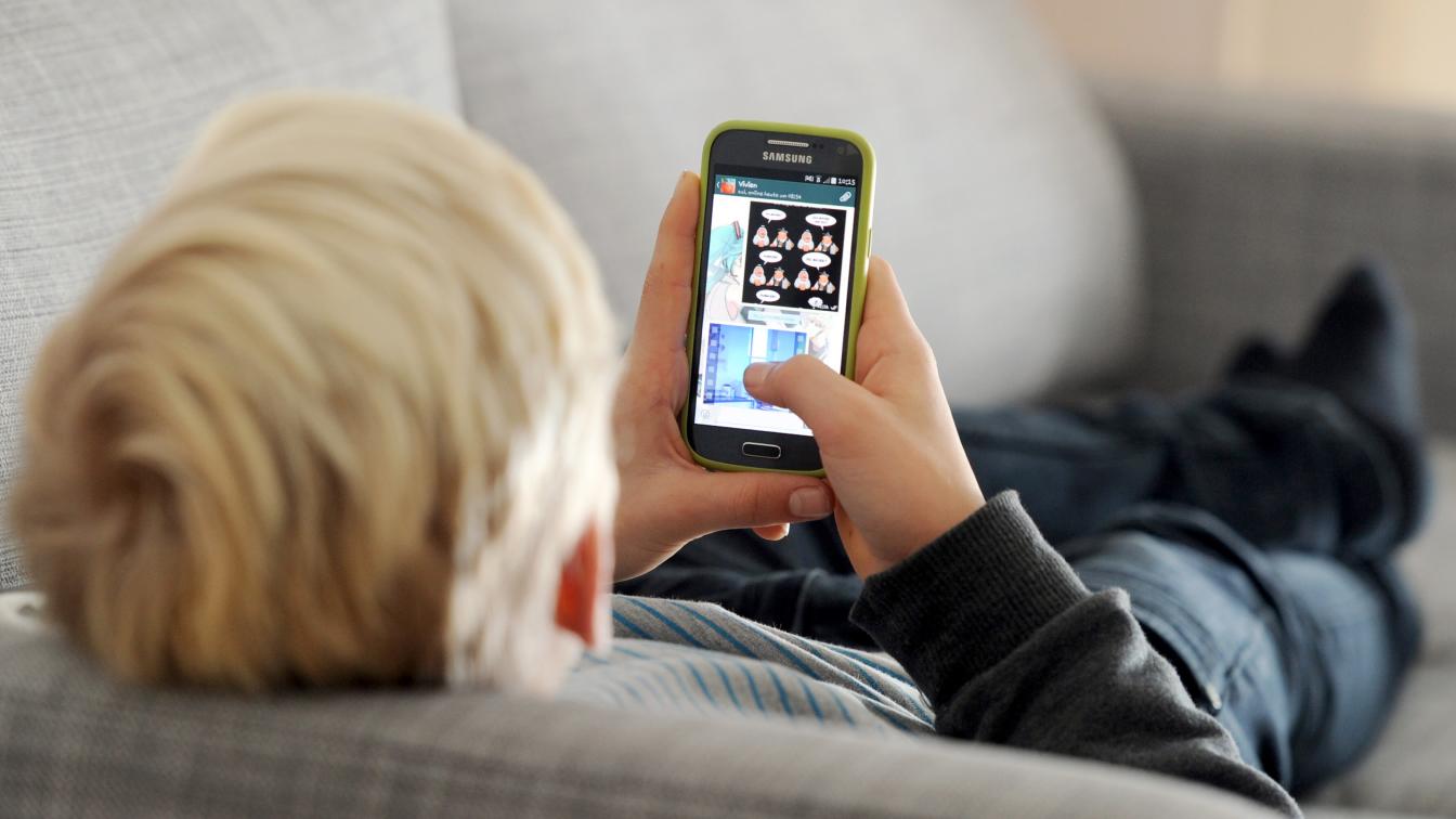 Ein Kind liegt auf einem Sofa und spielt am Smartphone