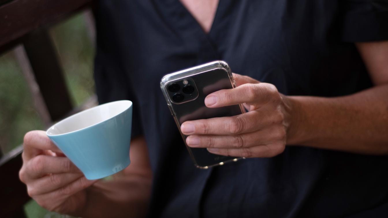 Eine Frau trinkt Kaffee und tippt etwas auf ihrem Smartphone