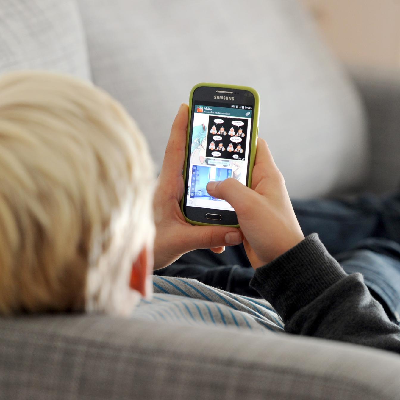 Ein Kind liegt auf einem Sofa und spielt am Smartphone