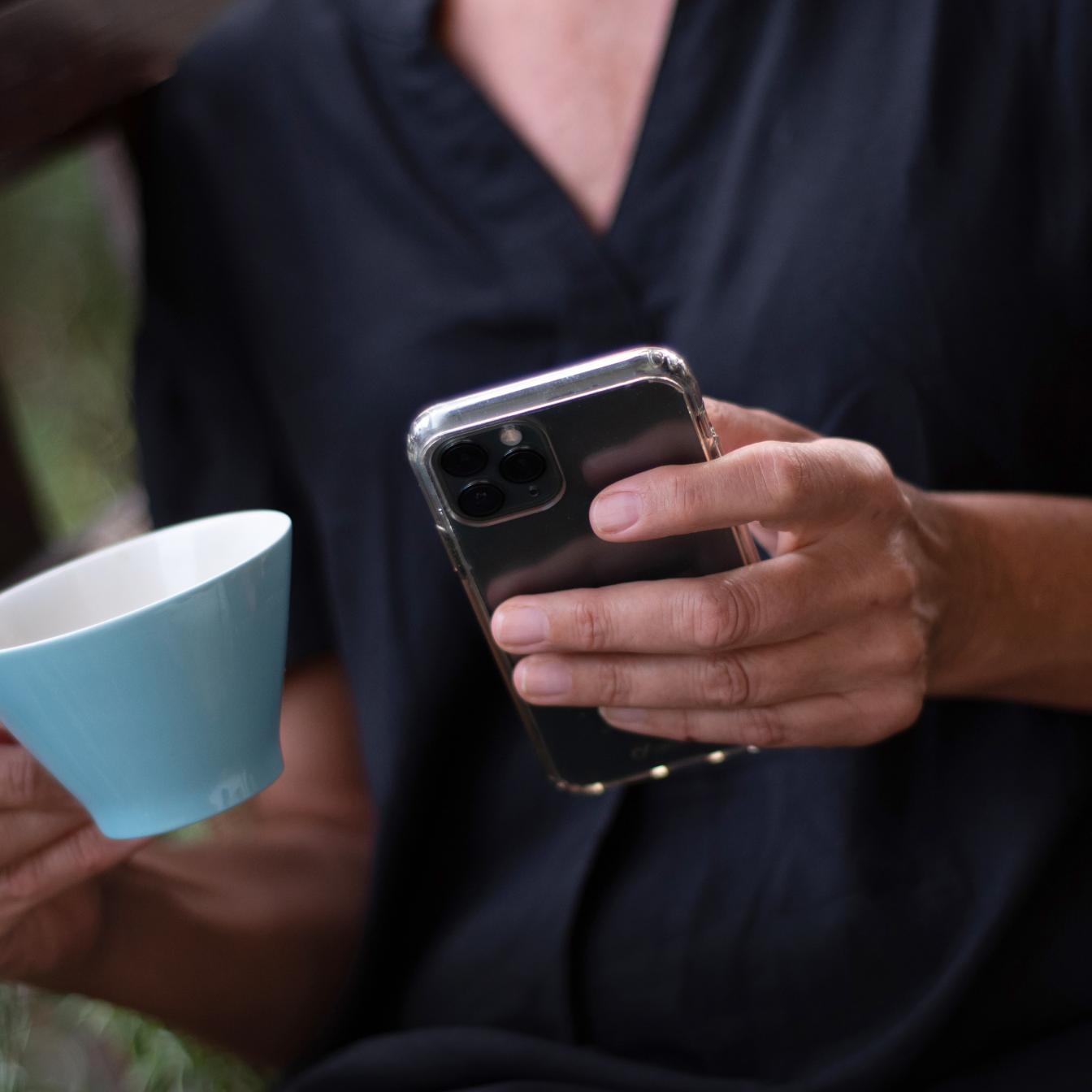 Eine Frau trinkt Kaffee und tippt etwas auf ihrem Smartphone